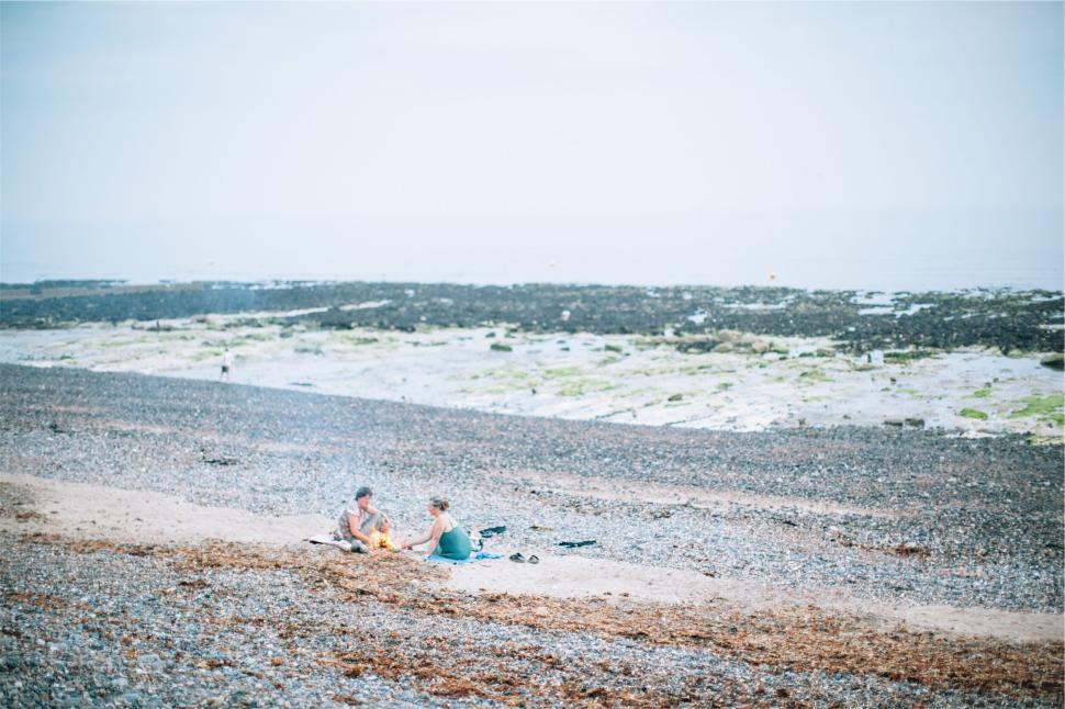 Free Image of Two People Relaxing on a Pebble Beach with Distant Tidal Flats 