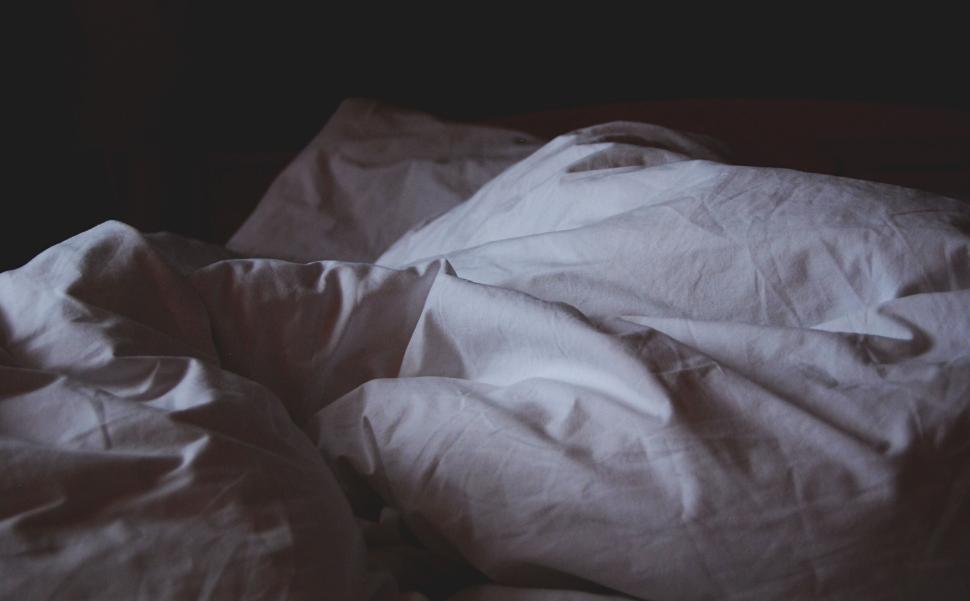 Free Image of Crumpled white bed linens in a dark room, rumpled and unmade. 