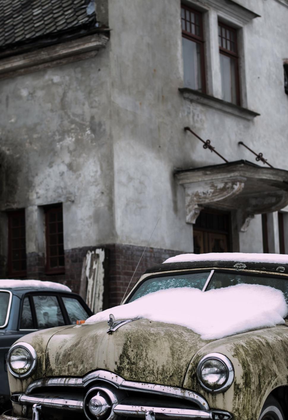 Free Image of Old cars covered in snow in front of a weathered building. 