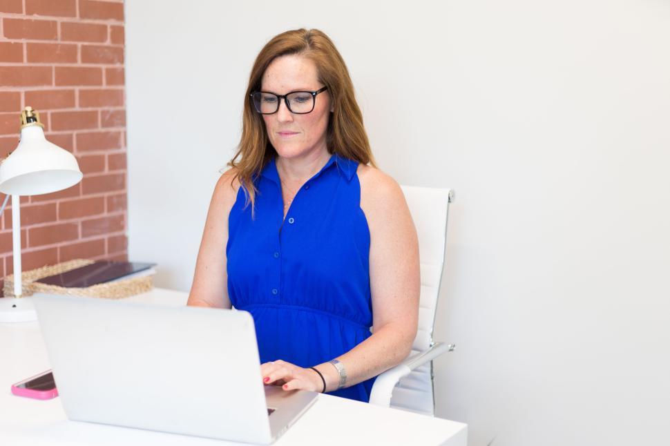 Free Image of Woman in blue dress working on laptop at modern office desk. 
