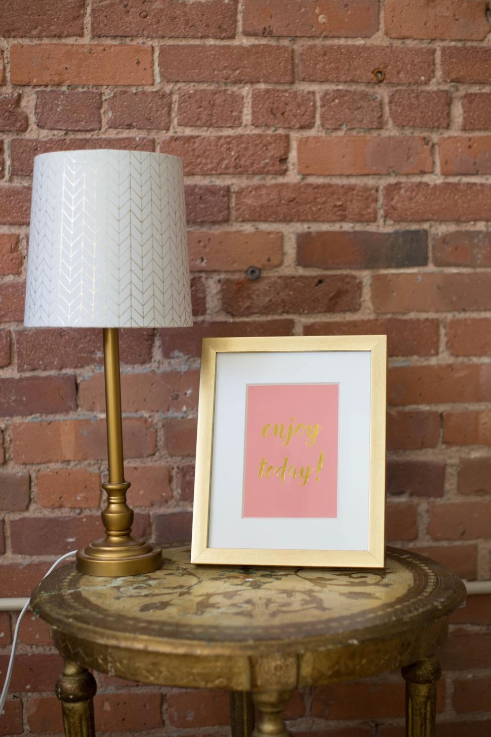 Free Image of Lamp and framed artwork on a vintage table against brick wall. 