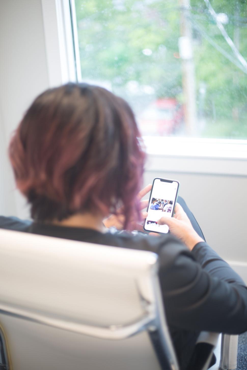 Free Image of Person using smartphone in white chair by window in daylight. 