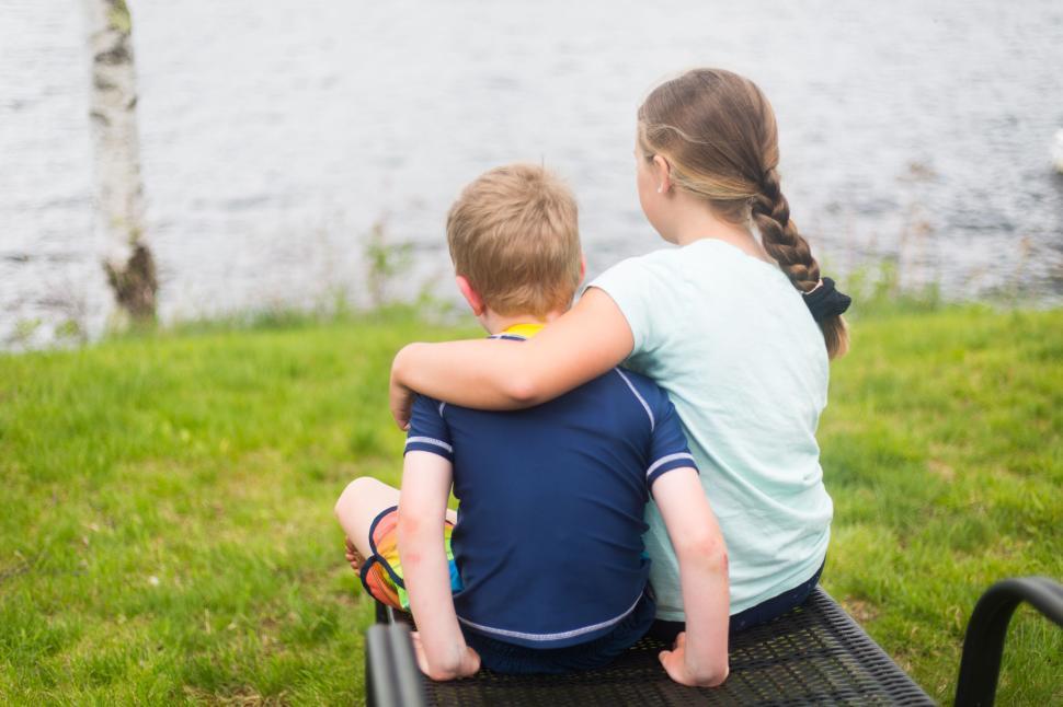 Free Image of Children sitting on the lakeside bench sharing a tender moment. 