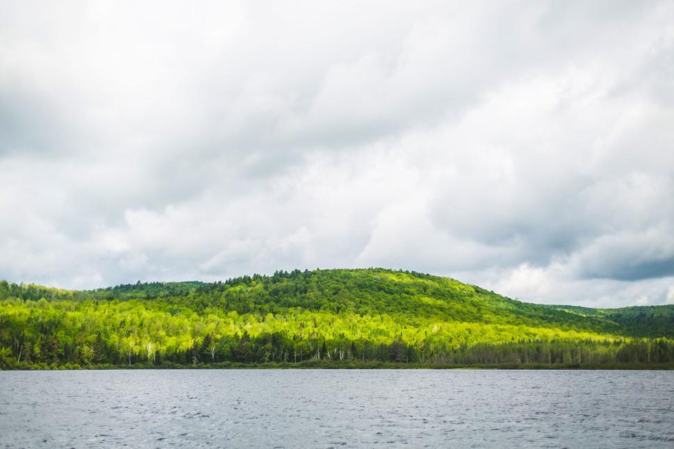 Free Image of Green hills and forest reflected in a lake under cloudy skies. 
