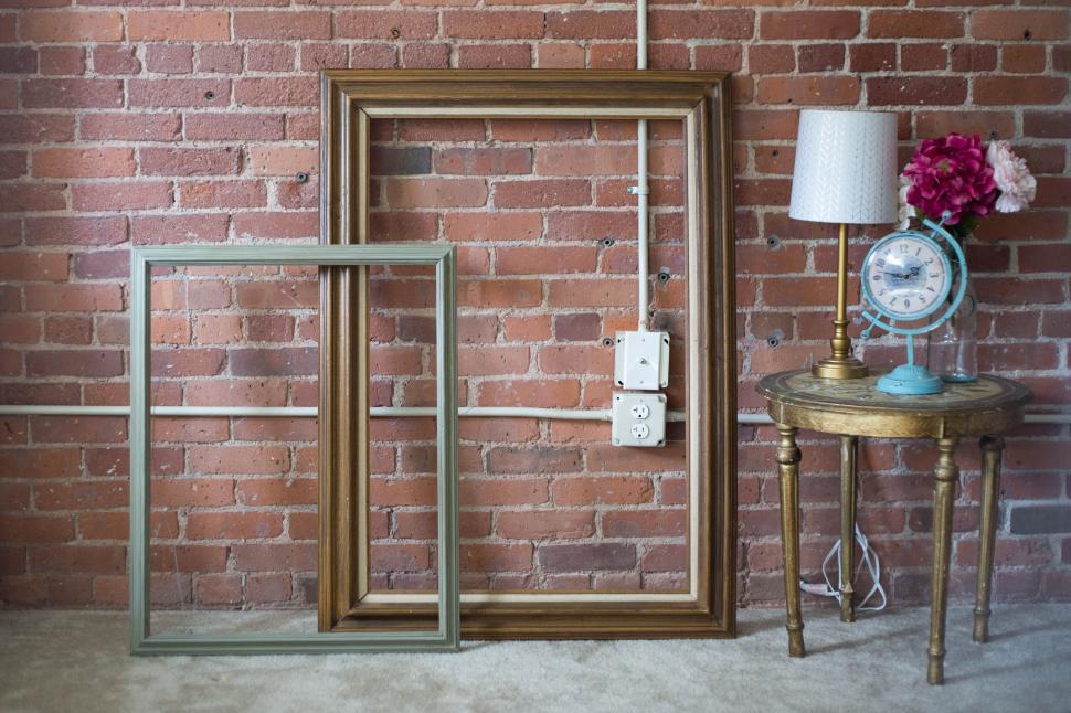 Free Image of Two empty picture frames near a vintage table against brick wall. 