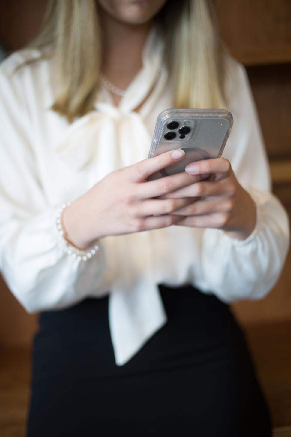 Free Image of Woman using a smartphone wearing a white blouse and pearl bracelet. 