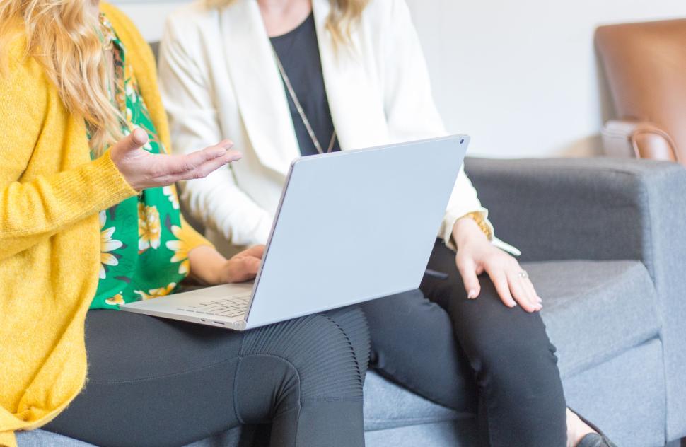 Free Image of Two women discussing work on a laptop while sitting on a couch. 