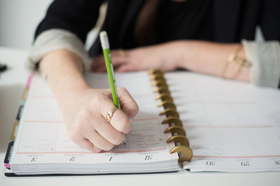 Free Image of Person writing plans in a spiral-bound planner with a green pencil. 