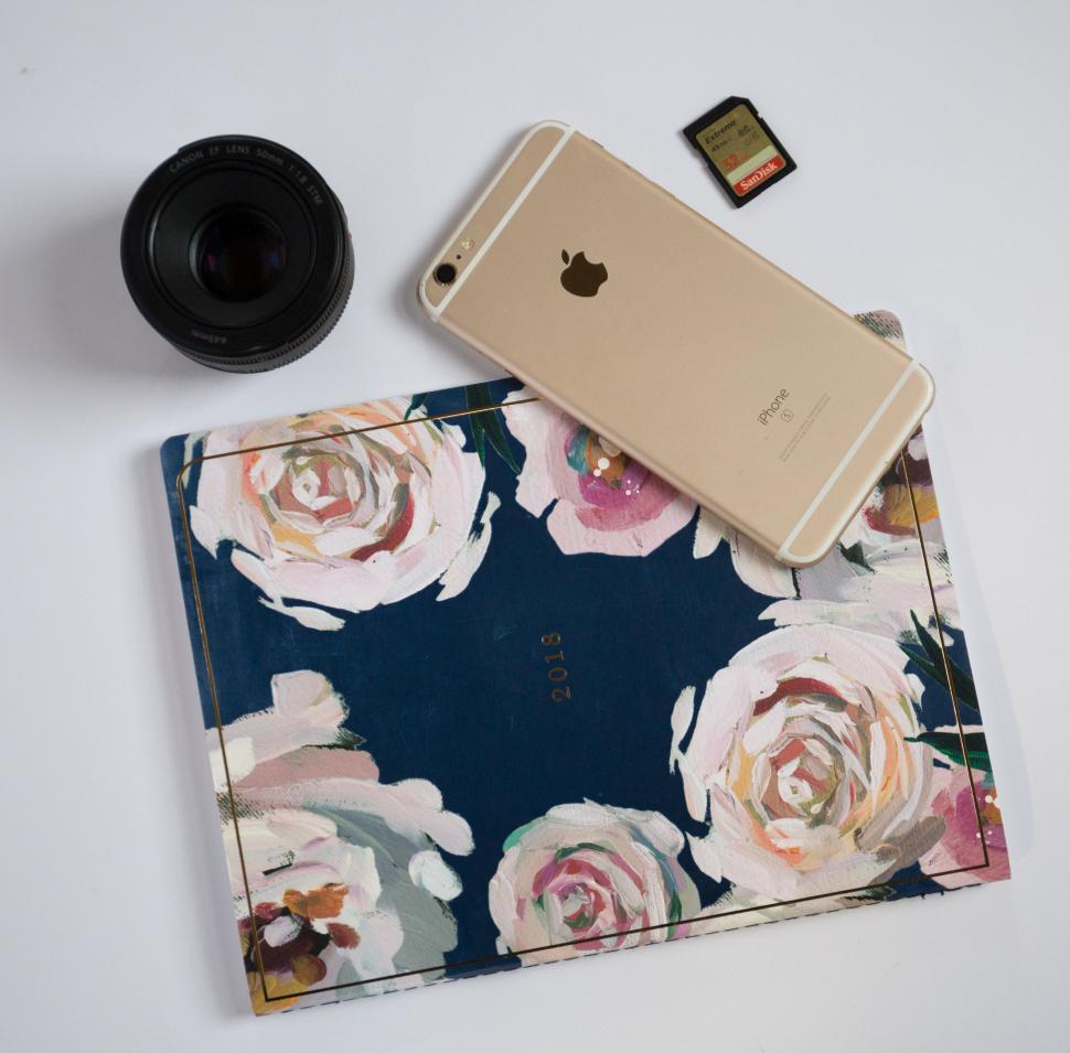 Free Image of Gold iPhone on Floral Notebook with Camera Lens and SD Card 