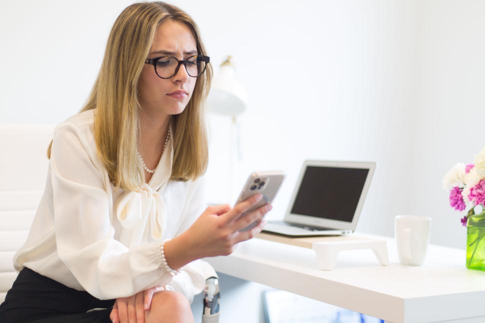 Free Image of Thoughtful young woman in glasses using smartphone in office 