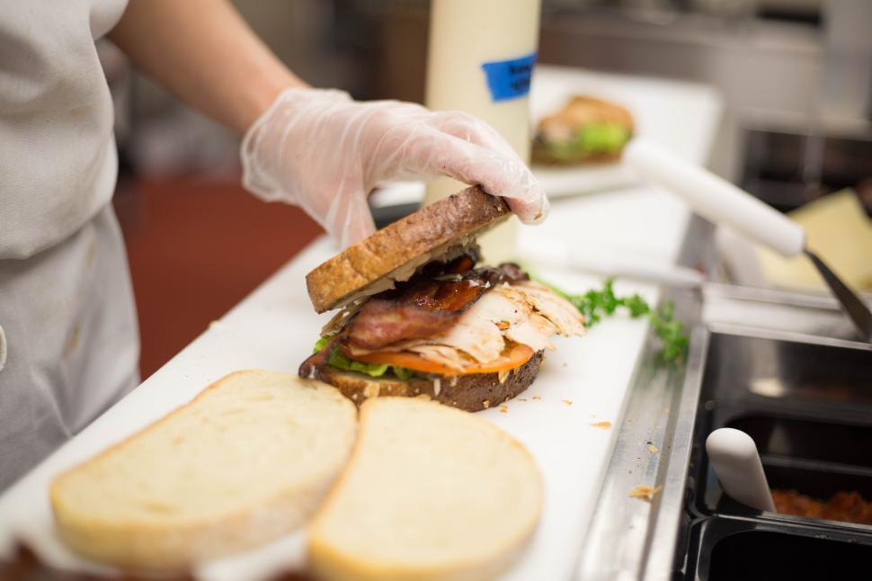 Free Image of Chef preparing a sandwich with gloves, placing ingredients carefully. 