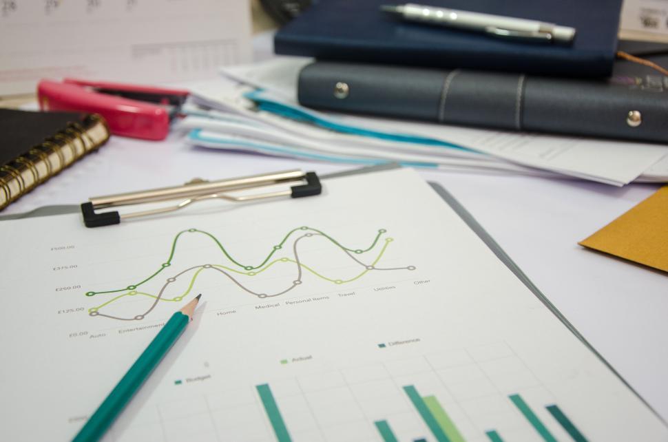 Free Image of A cluttered office desk with graphs, documents, and various office supplies. 