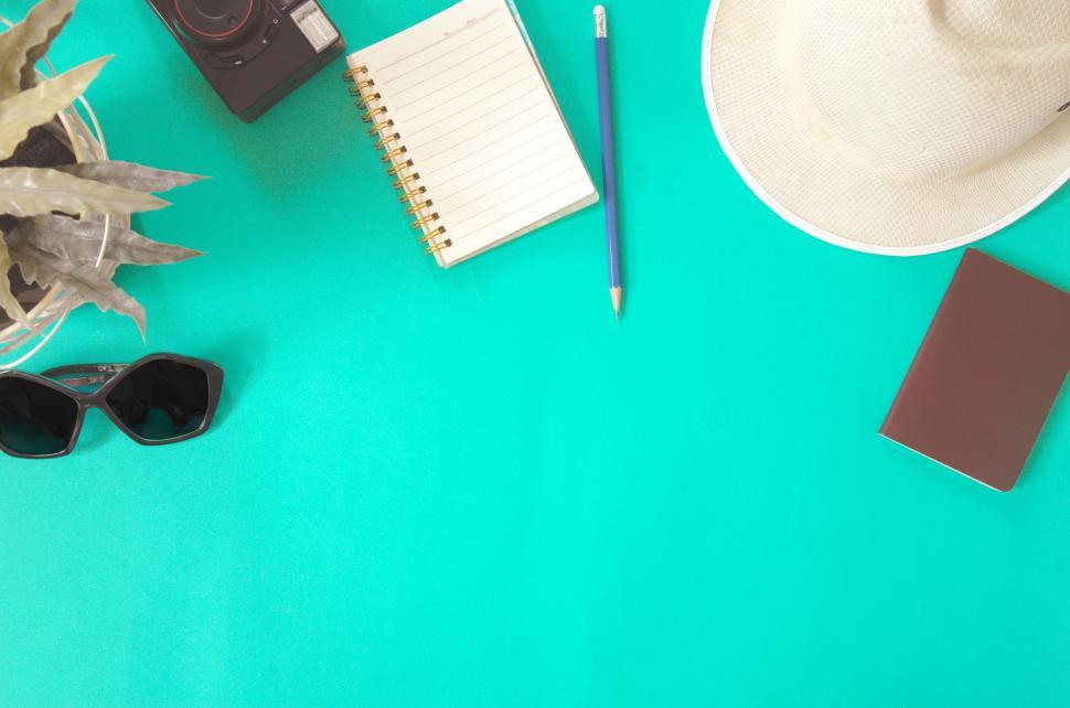 Free Image of Travel essentials including notebook, camera, hat on green surface. 