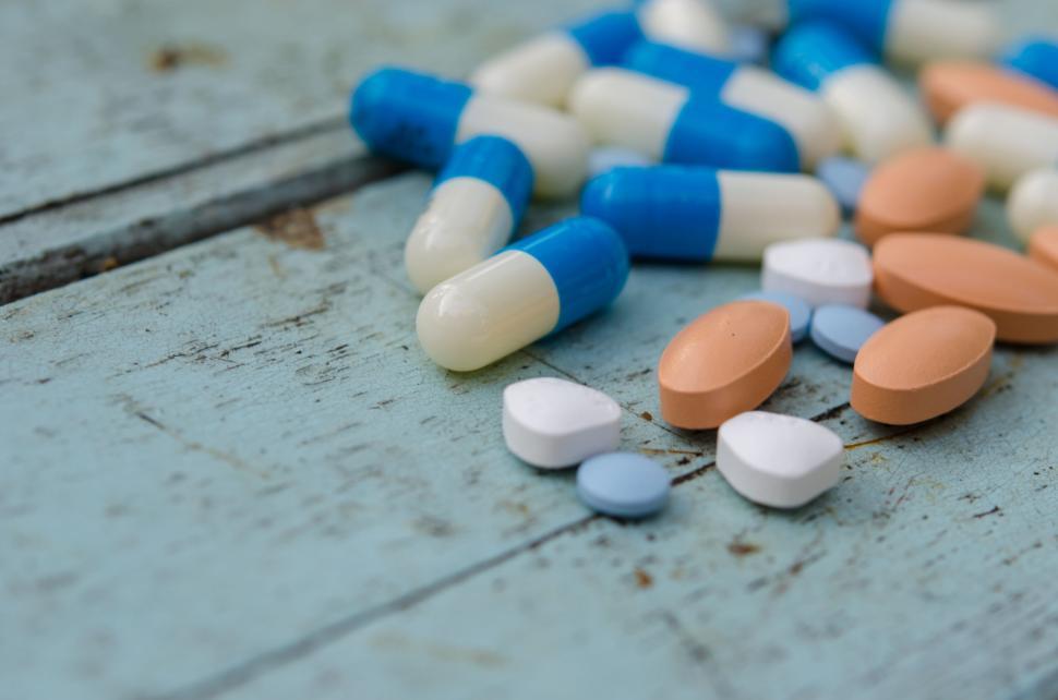 Free Image of Variety of medication pills and capsules scattered on wooden surface. 