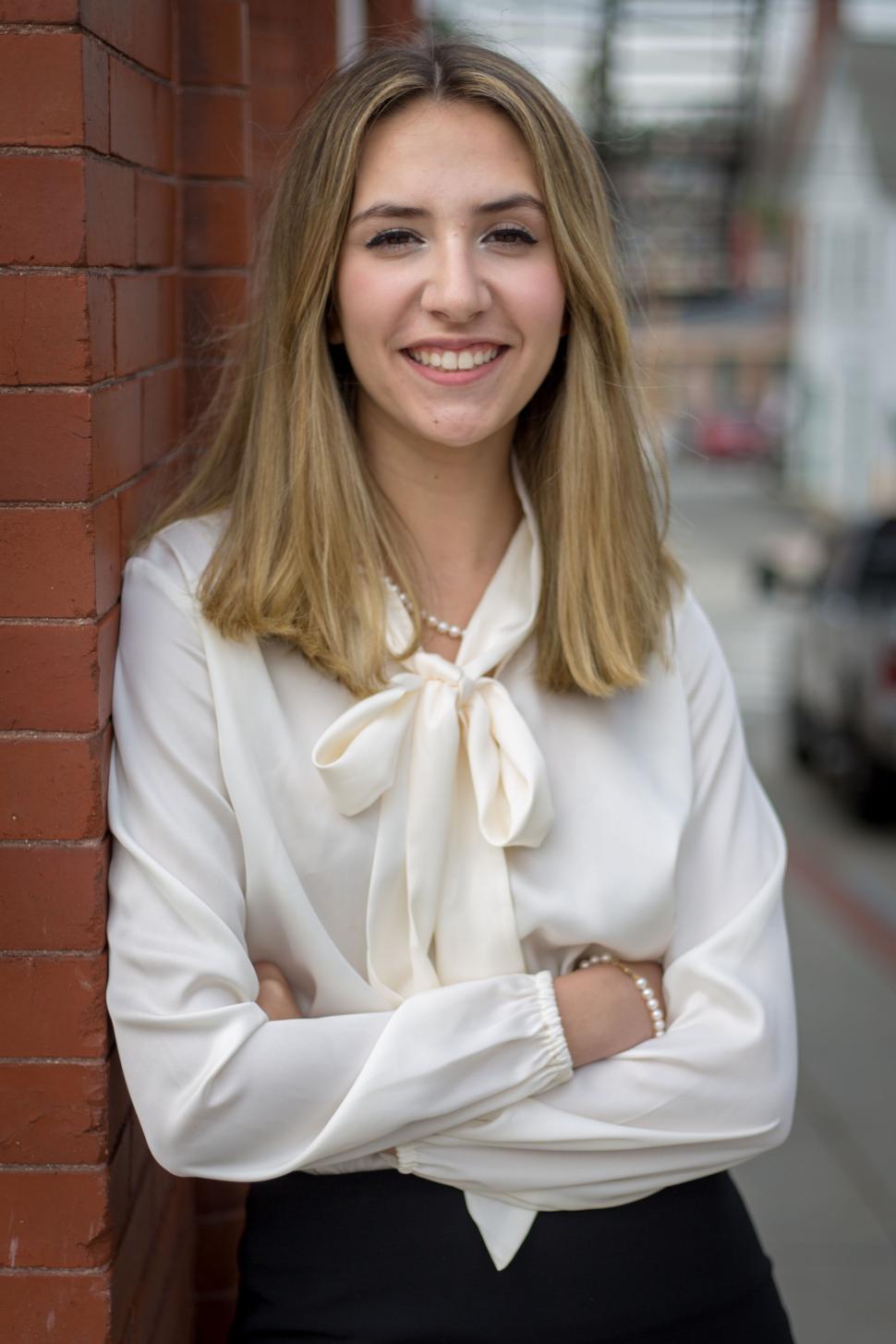 Free Image of Young woman confidently smiling in a white blouse, urban area 