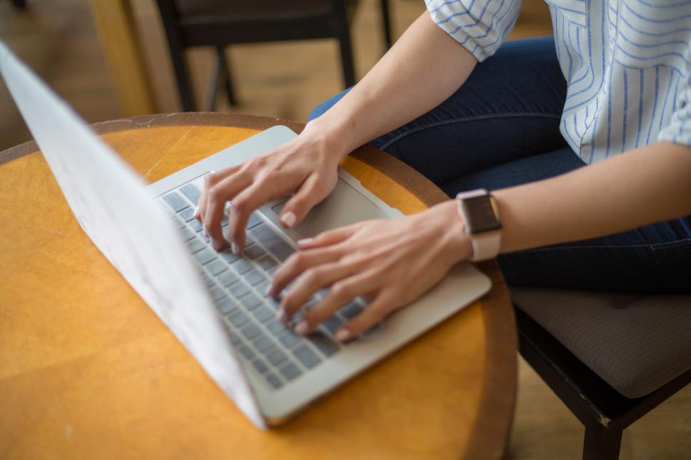 Free Image of Hands typing on laptop placed on round wooden table indoors 
