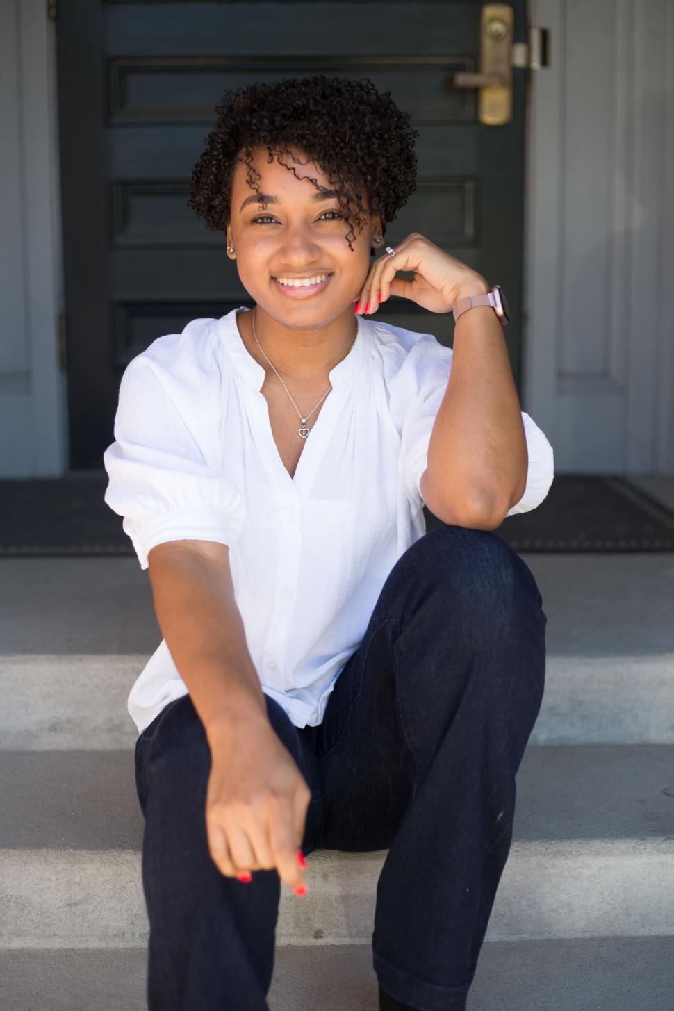 Free Image of Young woman sitting on steps smiling confidently in casual wear 