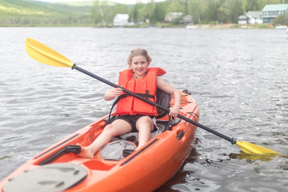 Free Image of Young girl kayaking on a lake with an orange kayak and paddle. 