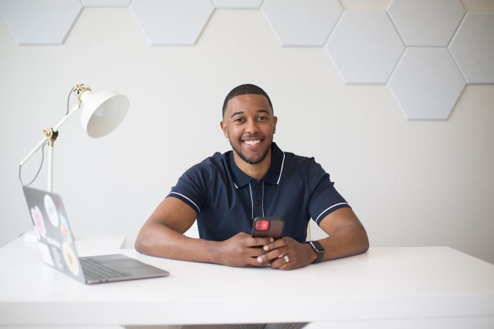 Free Image of Man in black shirt using smartphone, sitting at a white desk. 