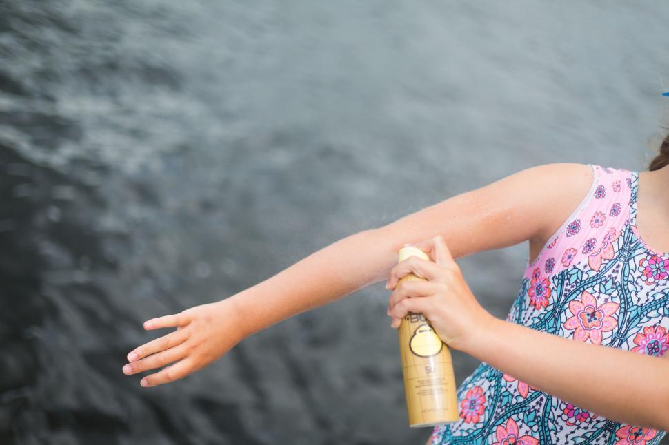 Free Image of Girl sprays her arm with insect repellent near water. 