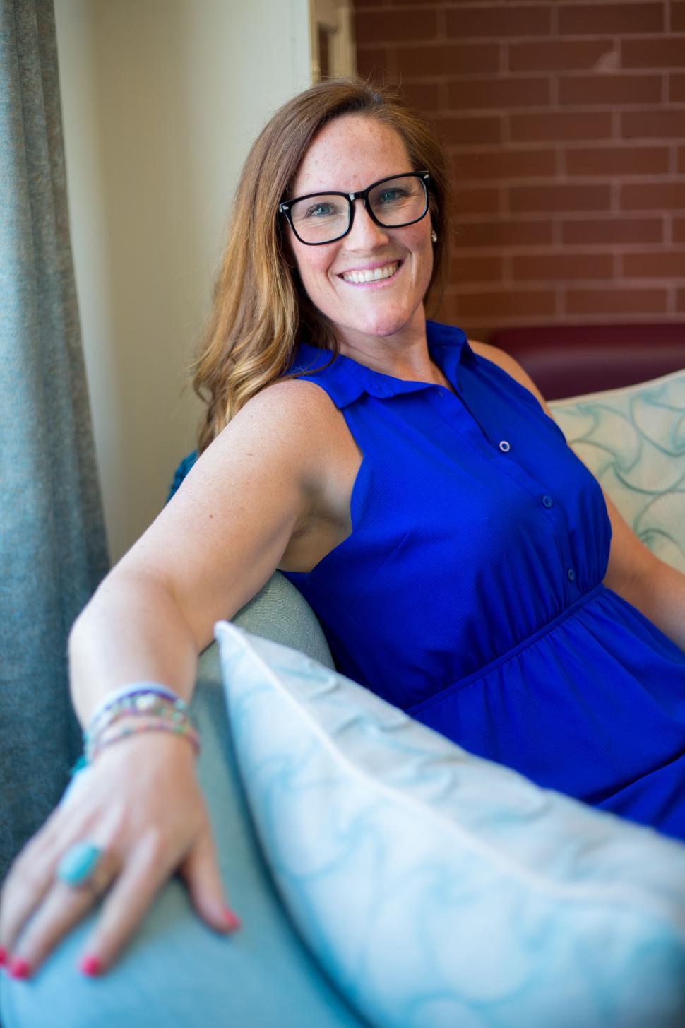 Free Image of Woman in blue dress sitting on a couch with patterned pillows. 
