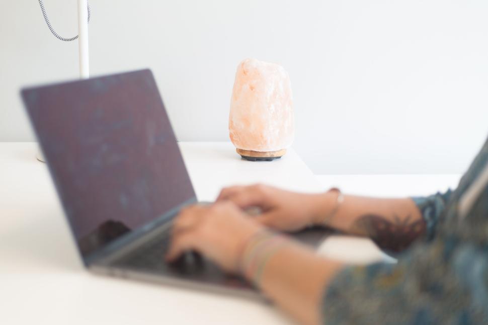Free Image of Person typing on a laptop with a Himalayan salt lamp on the desk. 