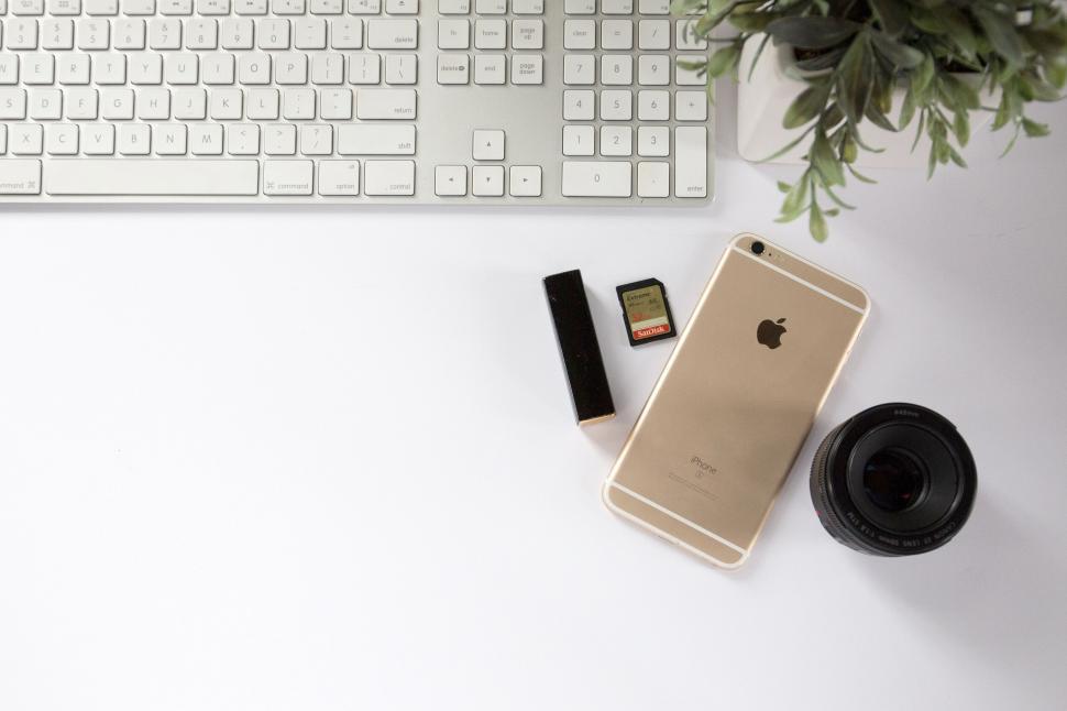 Free Image of White desk with Apple iPhone, memory cards, camera lens, keyboard. 