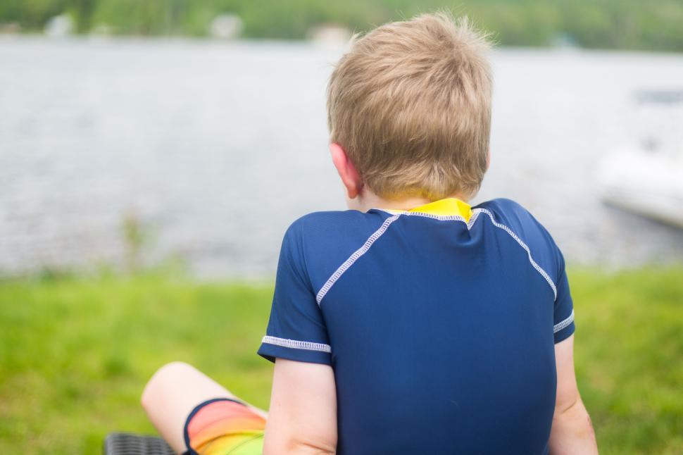 Free Image of Blond child in swimwear facing a tranquil lake, rear view 