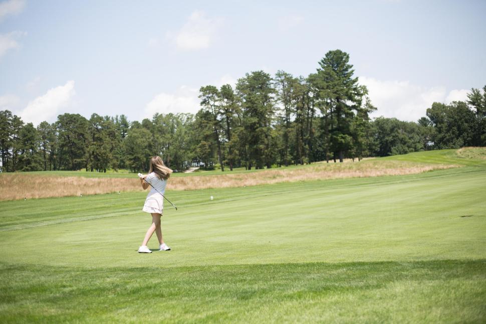 Free Image of Young girl playing golf in green field, mid-swing action shot 