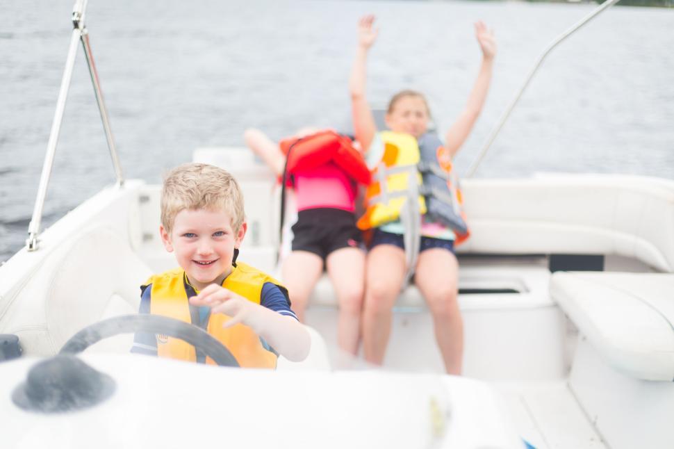 Free Image of Boy in life jacket steering a boat on a lake, two others relax. 