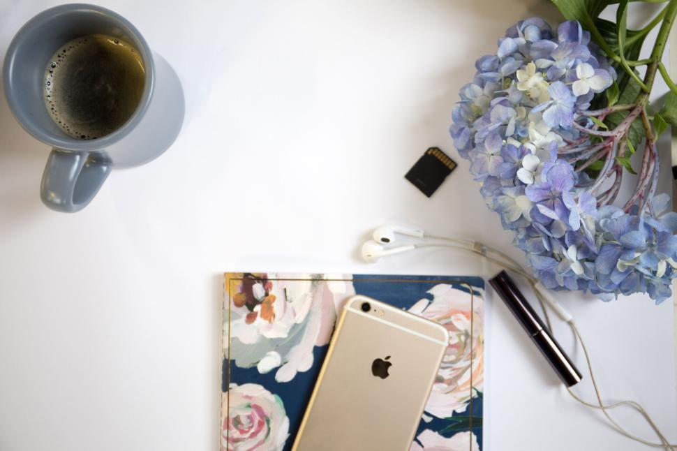 Free Image of Floral notebook, coffee, and iPhone with earphones by blue flowers 