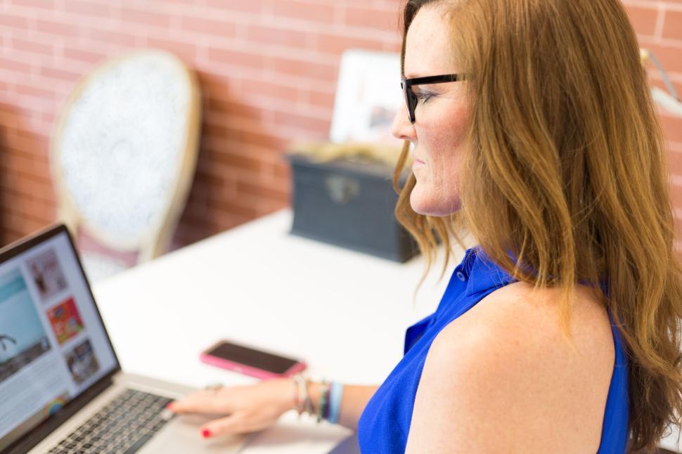 Free Image of Woman in blue top working on a laptop at a bright office space. 