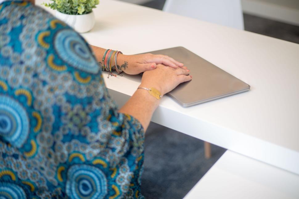 Free Image of Person with bracelet resting hands on closed laptop on white table. 