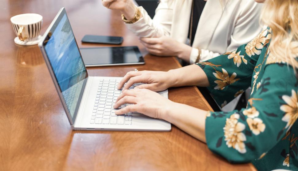 Free Image of Two women working on a laptop with a smartphone and tablet nearby. 