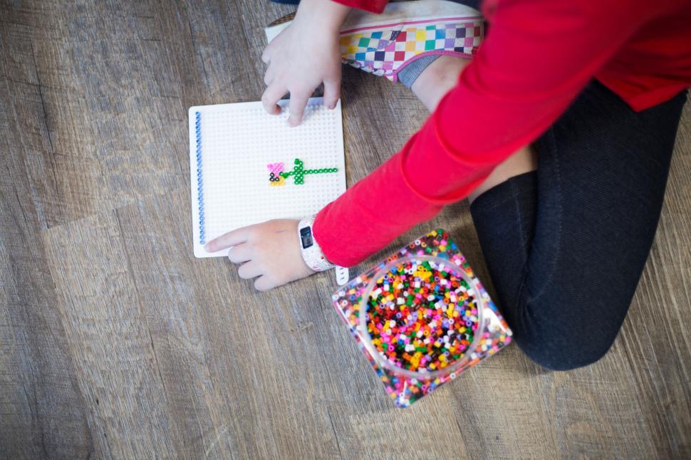 Free Image of Child creating a bead design on a pegboard with beads scattered around. 