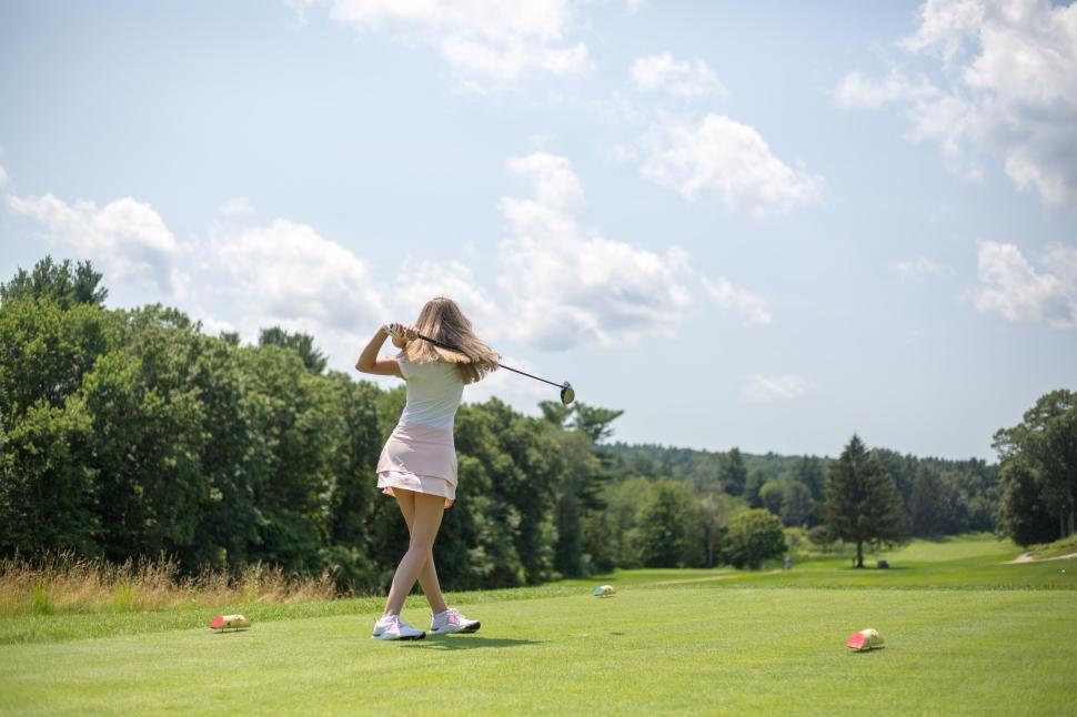 Free Image of Golfer in pink skirt taking a swing on a sunny golf course. 