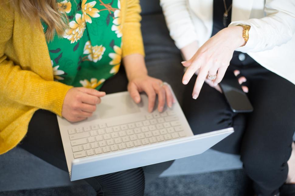 Free Image of Two women collaborating on a white laptop, one pointing at screen. 