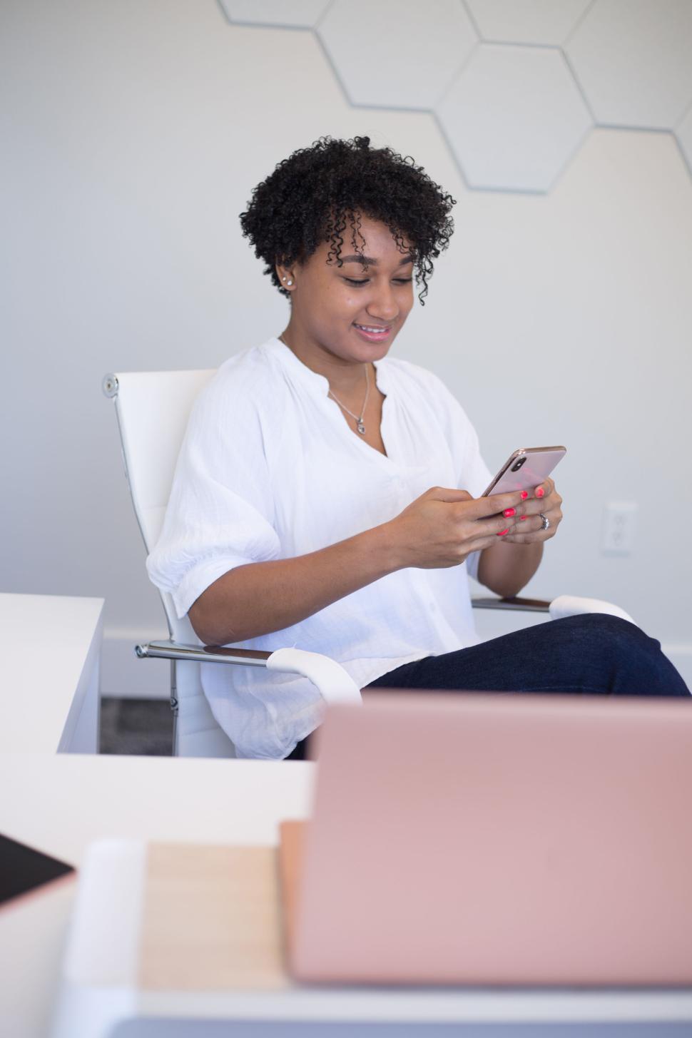 Free Image of Woman sitting in office chair texting on her smartphone indoors. 