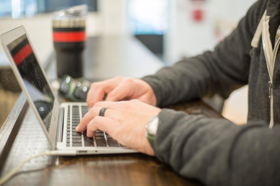 Free Image of Person typing on a laptop with a coffee tumbler in the background 