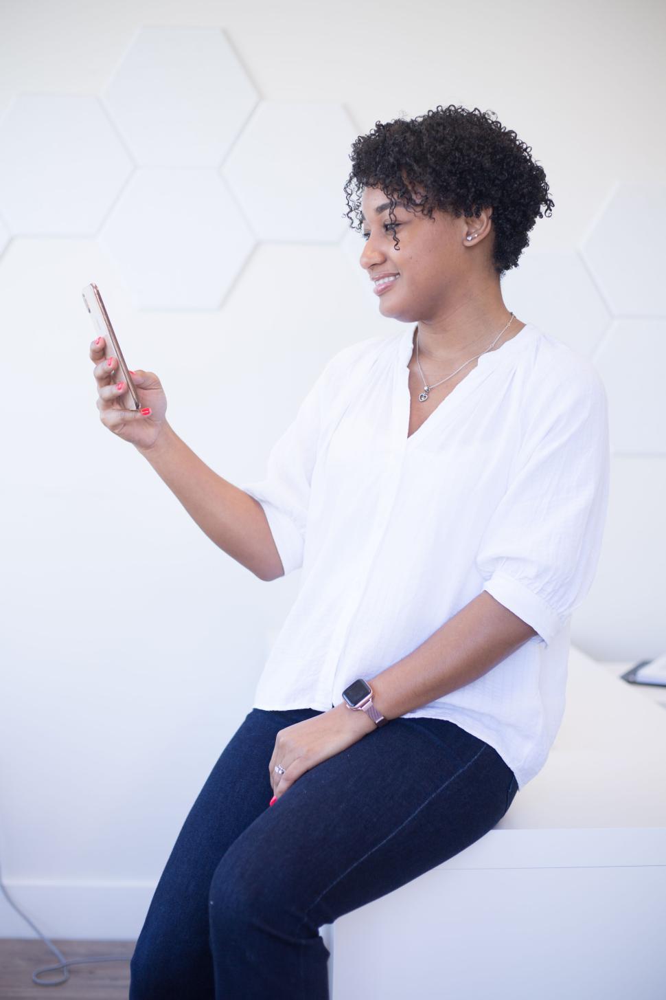 Free Image of Woman in white blouse using a smartphone in a bright, modern room 