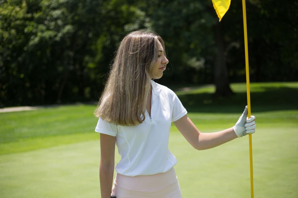 Free Image of Female golfer smiling by golf hole holding flag on course. 