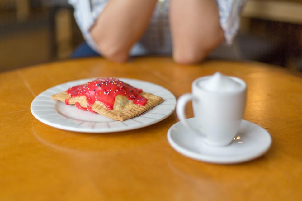 Free Image of Pop-tart on plate with coffee cup on wooden table, hands folded 