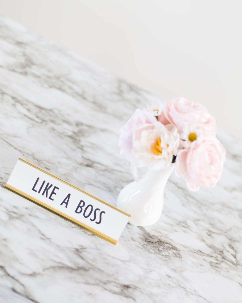 Free Image of Small vase with pink flowers and Like a Boss sign on marble surface 