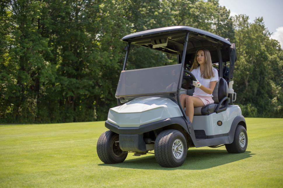 Free Image of Young woman driving golf cart across green, sunny golf course. 