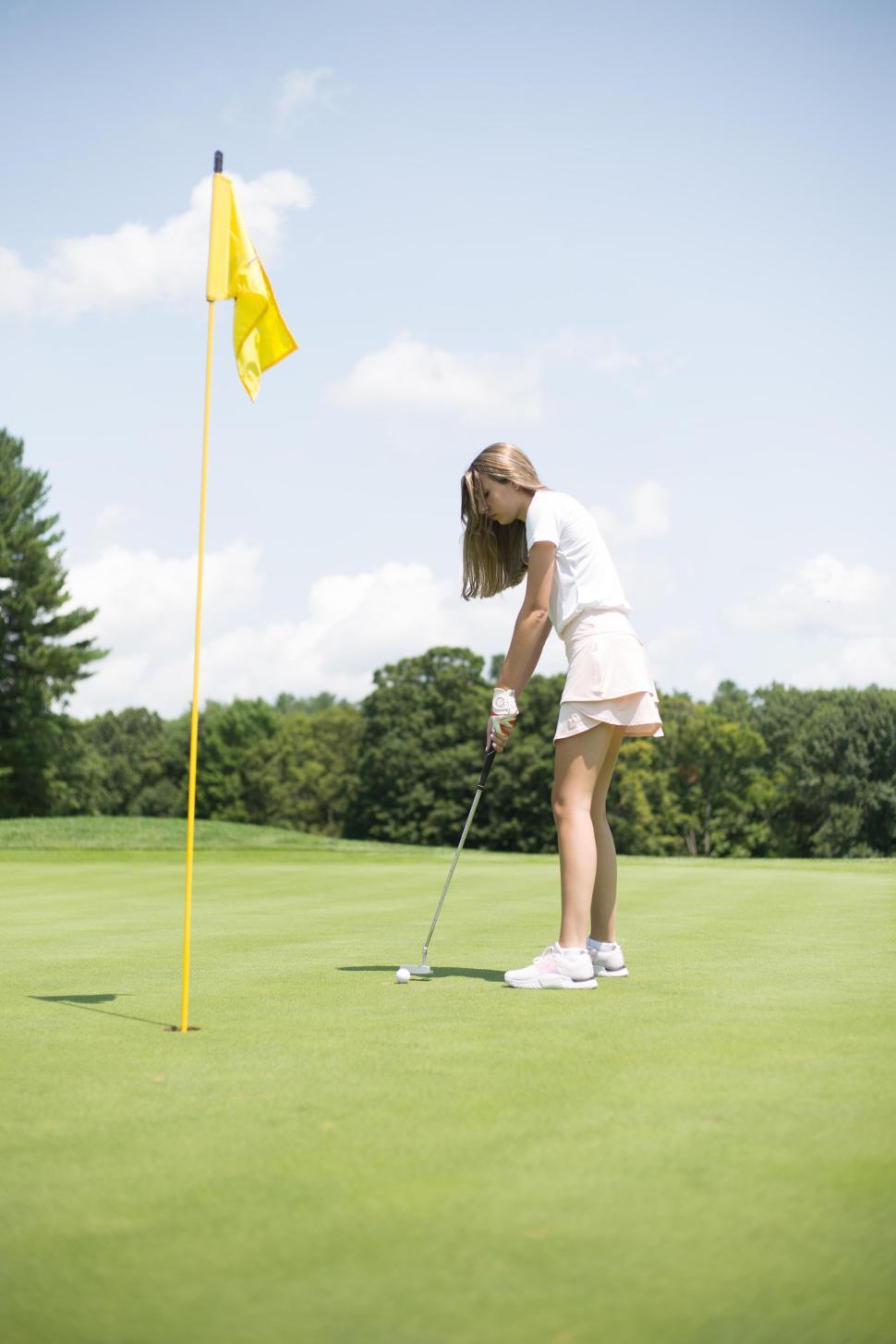 Free Image of Person playing golf on a sunny day, putting the ball into the hole 