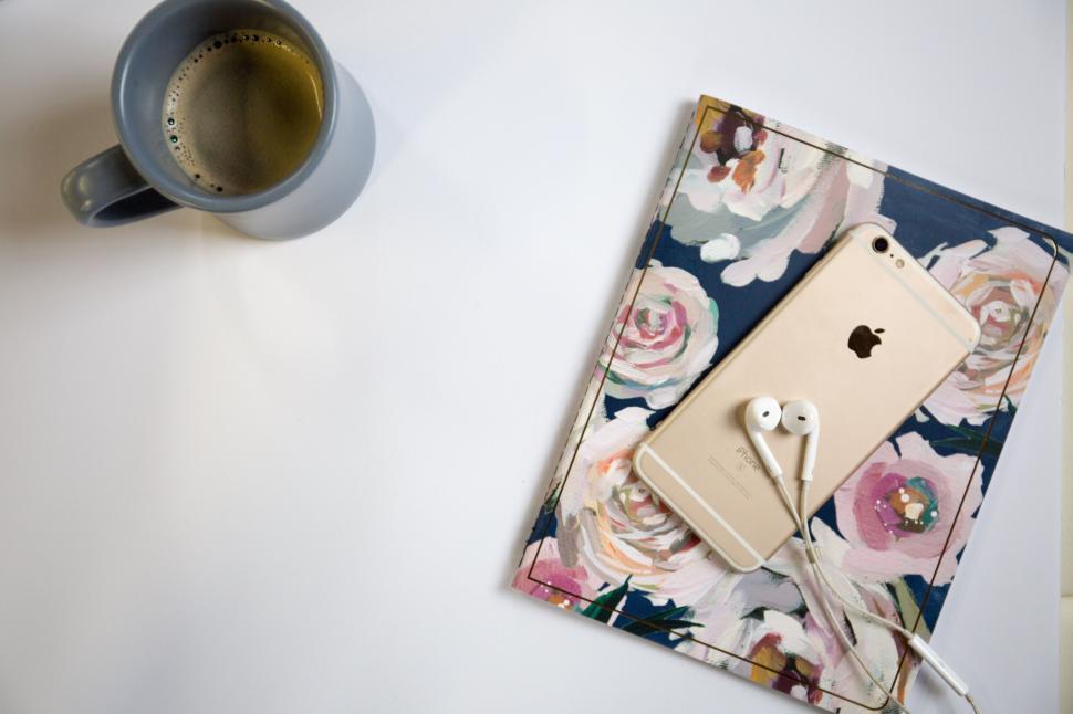 Free Image of Smartphone and earphones on floral planner beside coffee cup. 