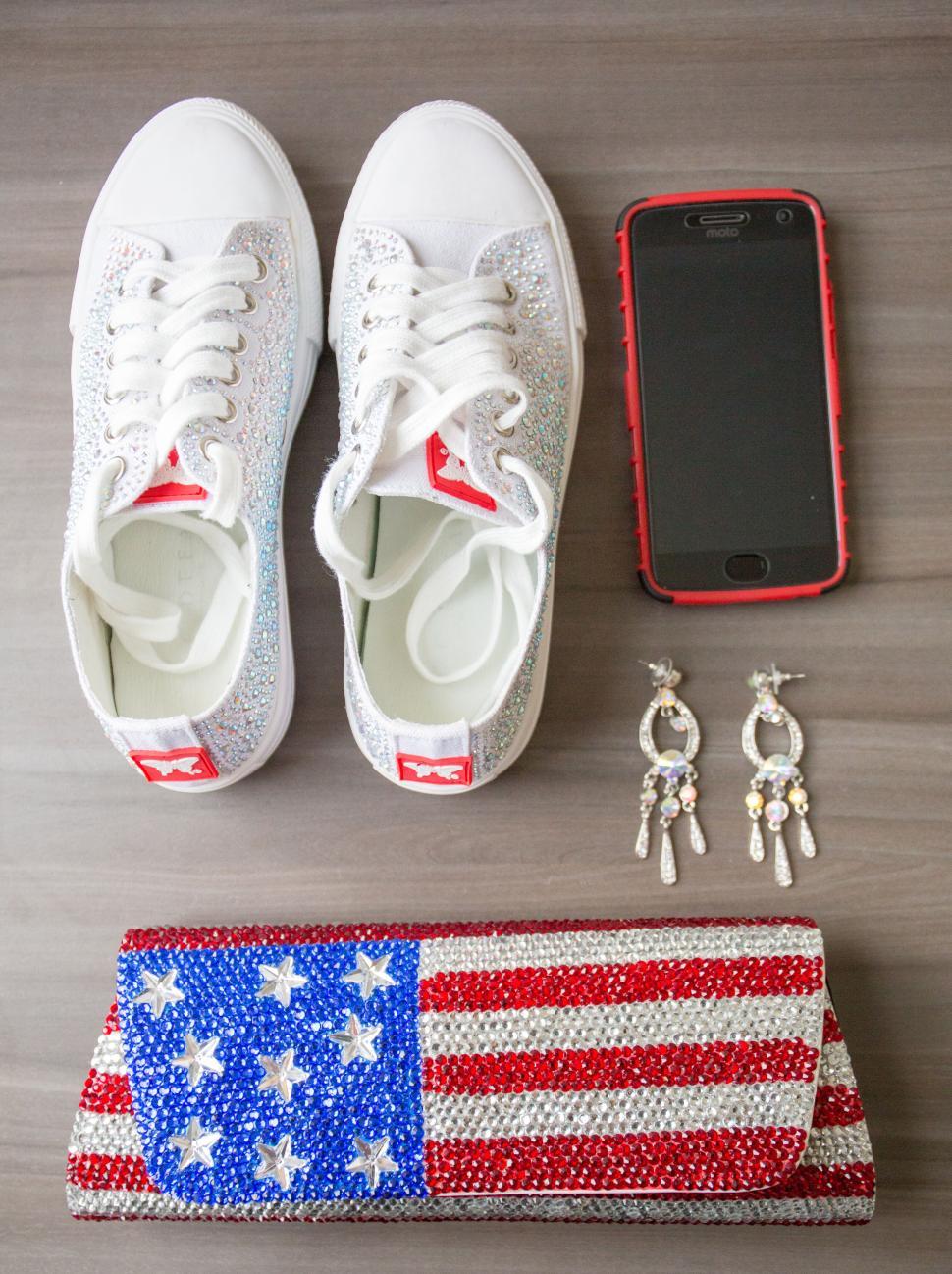 Free Image of White sneakers, earrings, phone, and USA flag bag on a table 