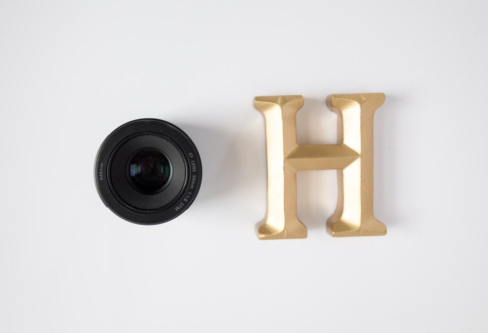 Free Image of Camera lens and golden H letter on a plain white background 