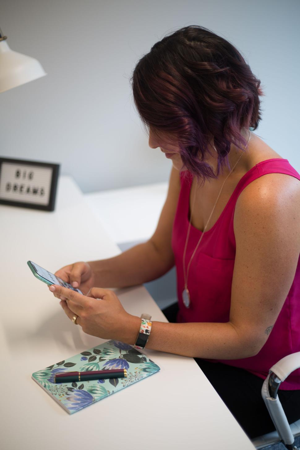 Free Image of Woman engaging with her smartphone at a clean, modern workspace. 