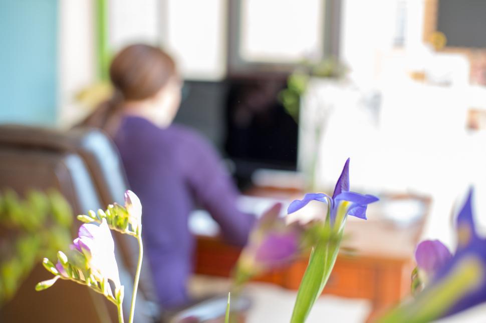 Free Image of Person working at desk with computer and vibrant flowers in foreground 